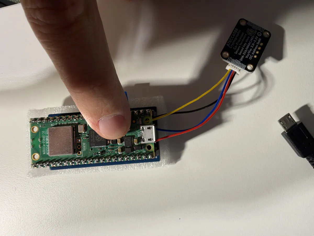 A finger pressing the small white BOOTSEL button on the Pico, the USB cable next to it